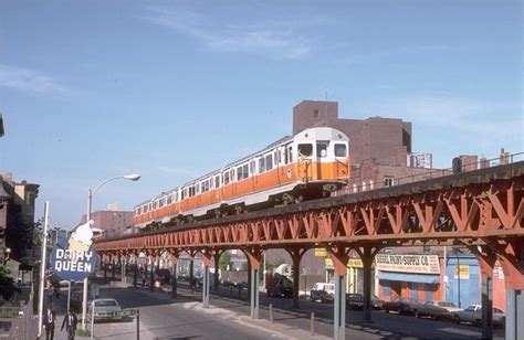 An Orange And White Train Traveling Over A Bridge Next To Tall