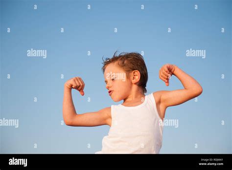 funny little kid showing his muscles on blue sky background with copy ...