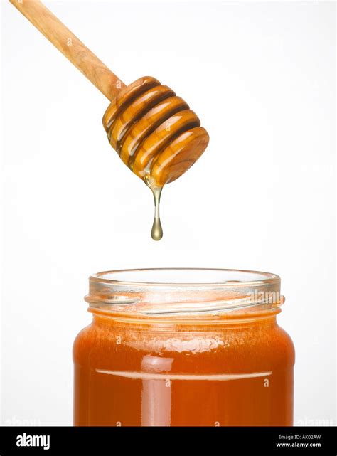 Honey Dripping From Wooden Honey Dripper Into Glass Jar Of Honey Stock