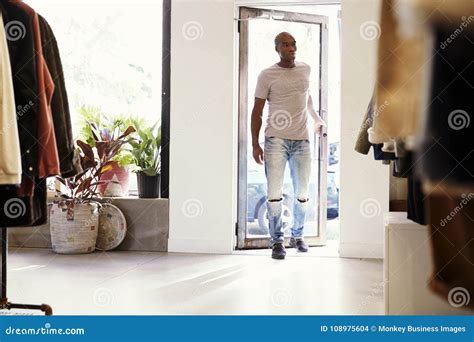 Young Black Man Walking Into A Clothes Shop And Closing Door Stock