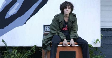 a man sitting on top of a piece of luggage in front of a building with a mural behind him