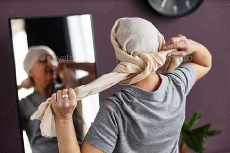 Back View Of Mature Bald Woman Tying Headscarf Looking In Mirror Stock