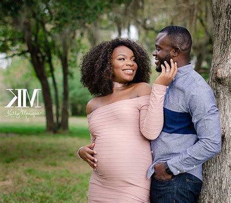 A Pregnant Woman Leaning Against A Tree While Holding Her Husband S