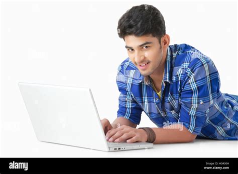 Happy Indian Man Lying On Floor Using A Laptop Pc Looking At Camera