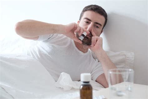 Man Feeling Cold And Using A Nasal Spray Lying In The Bed Stock Photo