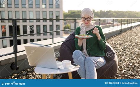 Lady Holding Plate With Food While Typing On Laptop Outside Stock