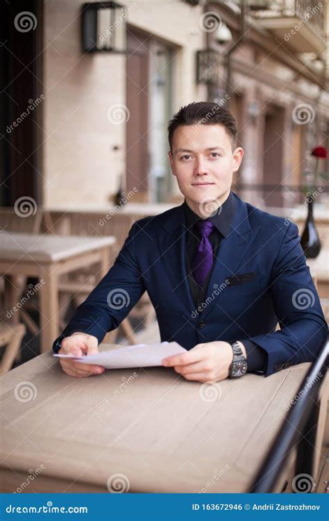 A Friendly Businessman In A Suit Is Sitting At A Table In A Cafe He