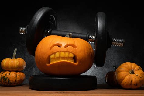 Halloween Gym Concept With Carved Pumpkin Lifting Dumbbells Weight Workout And Sport Training