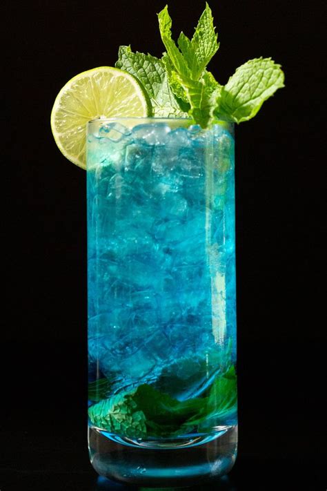 A Blue Drink With Lime And Ice In A Tall Glass On A Black Table Top