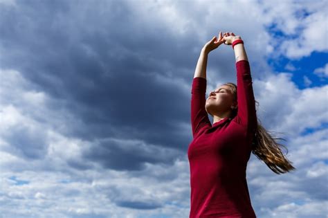 Chica joven alegre sobre un fondo de cielo con nubes levantó las manos