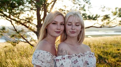 Two Cute Blonde Girlfriends In Identical Dresses Posing For The Camera