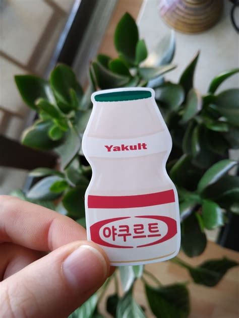 A Person Holding Up A Small Plastic Bottle With The Word Yakult On It