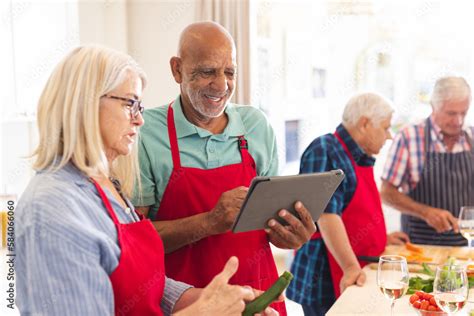 Happy Group Of Diverse Senior Friends In Aprons Using Tablet During