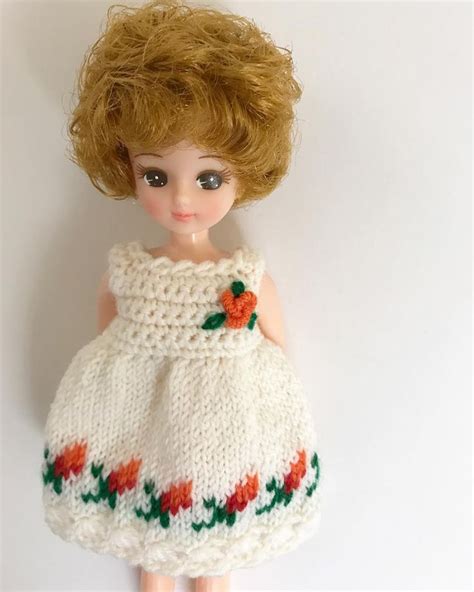 A Doll With Blonde Hair Wearing A White Knitted Dress And Red Flowered