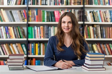 Souriante Jeune Fille Assise à Un Bureau Dans La Bibliothèque Avec Un