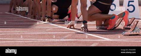 Group Of Male Track Athletes On Starting Blocks Hands On The Starting