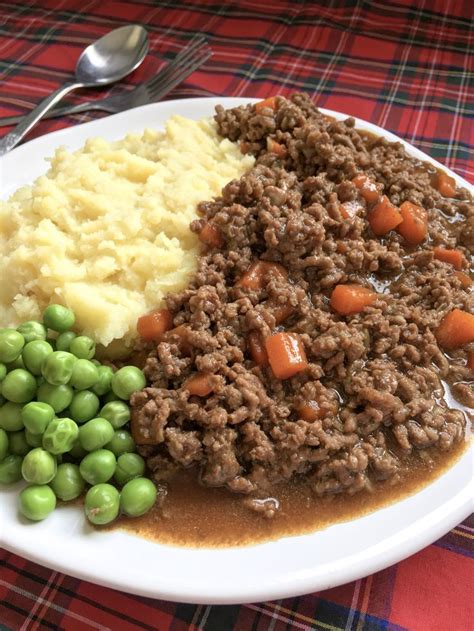 A White Plate Topped With Meat Potatoes And Peas