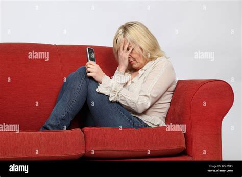 Blonde Woman Sitting On A Red Sofa Holding Her Phone Stock Photo Alamy