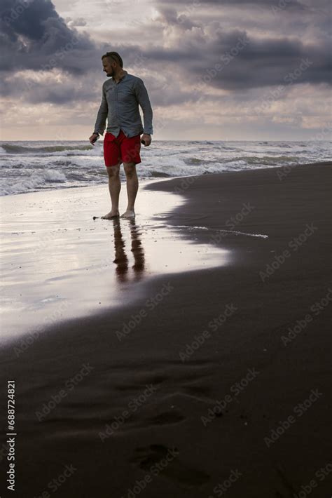 A Man Walks On The Black Sand Stormy Sea With Waves Dangerous For