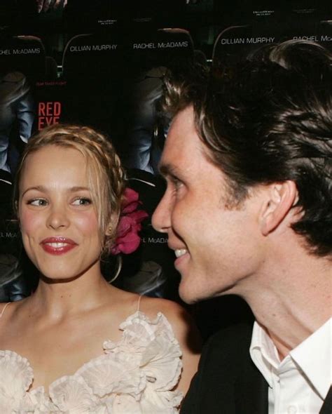 Two People Standing Next To Each Other In Front Of A Red Carpeted Wall