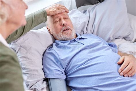 Woman Checking Fever Temperature Of Senior Sick Man Lying On Bed Stock