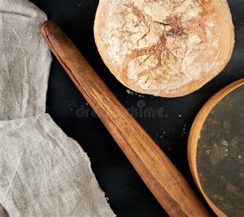 Round Baked Bread And Wooden Old Rolling Pin On A Black Table Stock