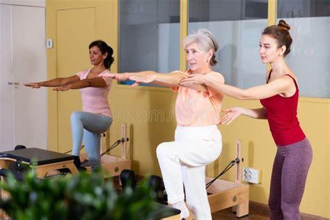 Trainer Controlling Movements Of Senior Woman Doing Pilates On Combo