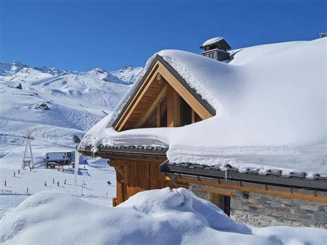 The Roof Of A House Covered In Snow With Mountains In The Background