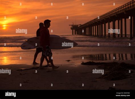 Hombre caminando en la playa llevando tablas de surf fotografías e