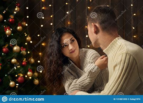 Young Couple In Christmas Lights And Decoration Dressed In White Fir Tree On Dark Wooden