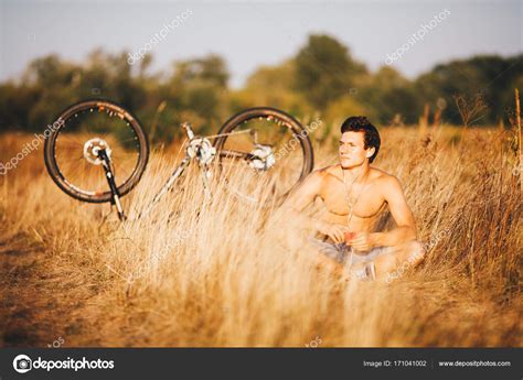 A Handsome Muscular Guy With A Naked Torso Sitting Near A Bicycle In The Countryside In A Field