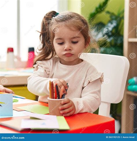 Adorable Hispanic Girl Student Sitting On Table Drawing On Paper At