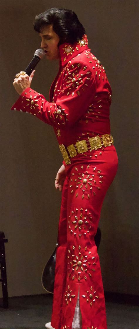 The Man Is Dressed In Red And Singing Into A Microphone While Wearing An Elvis Costume