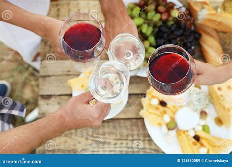 Friends Holding Glasses Of Wine Over Picnic Table At Vineyard Stock