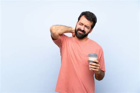 Joven con barba sosteniendo un café para llevar sobre pared azul