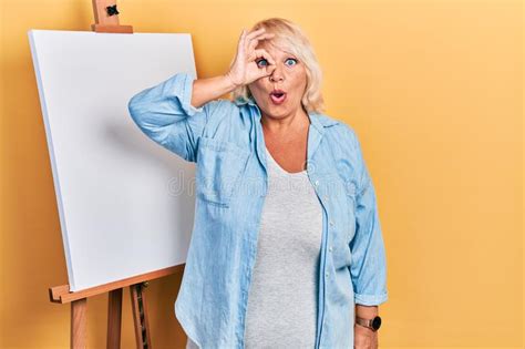 Middle Age Blonde Woman Standing By Painter Easel Stand Doing Ok