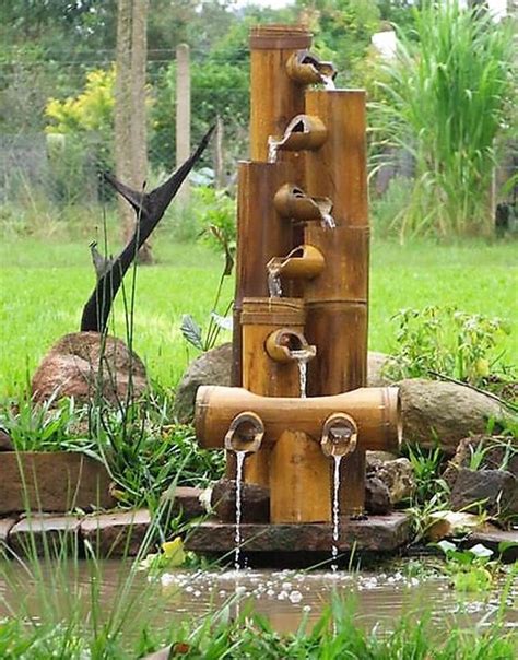 a water fountain made out of bamboo sticks and other items in a garden with green grass