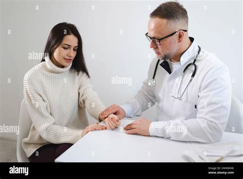 Male Doctor Measuring Pulse Of Young Female Patient In Clinic Woman On