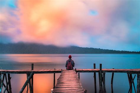 Man Sitting On A Dock By The Lake At Sunset Sky Stocksy United