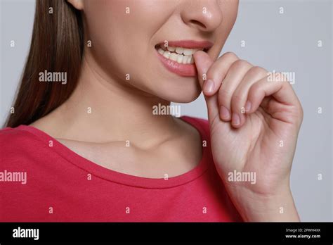 Young Woman Biting Her Nails On Light Grey Background Closeup Stock