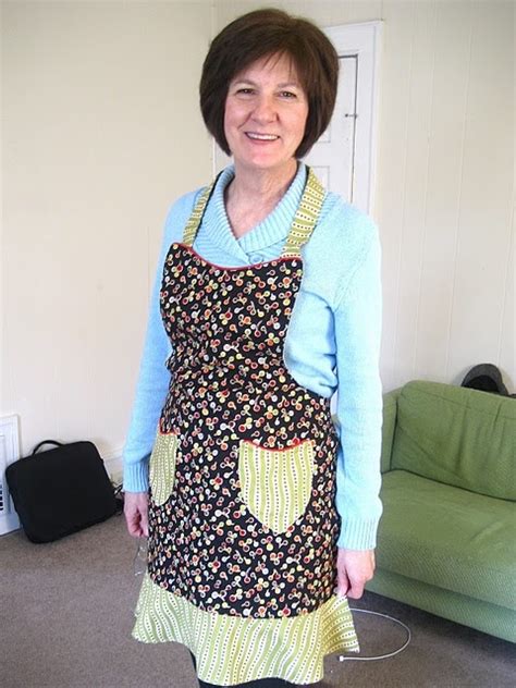 A Woman Wearing An Apron Standing In Front Of A Green Couch With Her