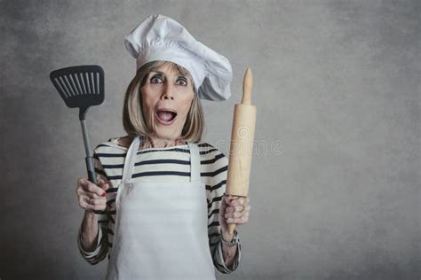 Surprised Senior Woman With Cook Hat And Rolling Pin And Spatula Stock