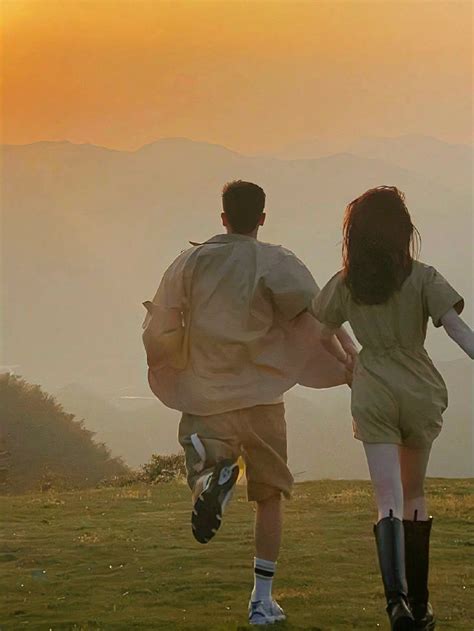 A Man And Woman Running In The Grass With Mountains In The Backgrouds