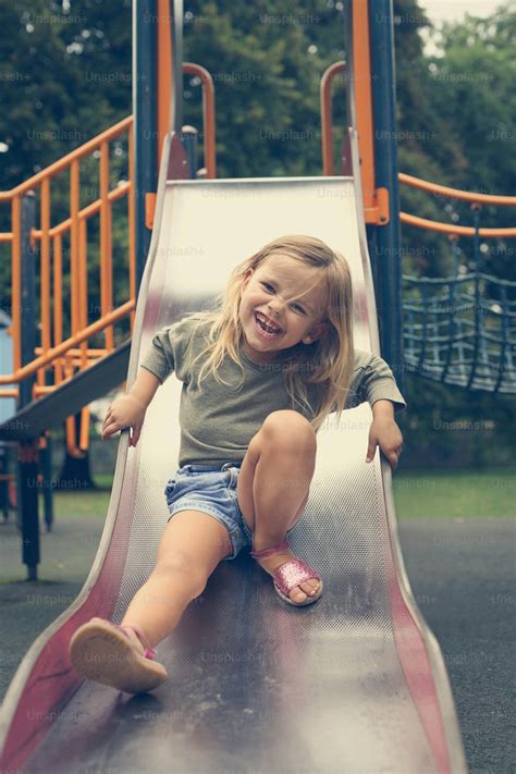 Foto Zum Thema Kleines Mädchen Rutscht Eine Rutsche Auf Einem Spielplatz Hinunter Bild Zu