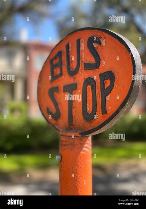 A Vertical Shot Of An Orange Round Bus Stop Sign With Black Letters