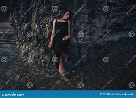 Seductive Girl In The Black Dress Standing Leaning Against The Rock