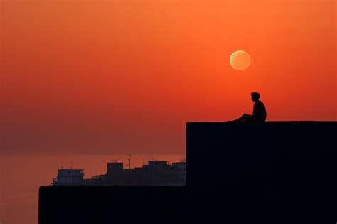 Premium AI Image | silhouette of a person sitting on a ledge at sunset