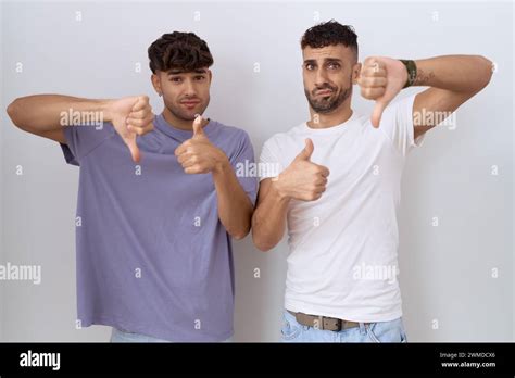 Homosexual Gay Couple Standing Over White Background Doing Thumbs Up And Down Disagreement And