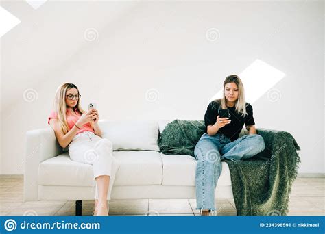 Two Women Sitting On Sofa In Living Room And Using Mobile Phones