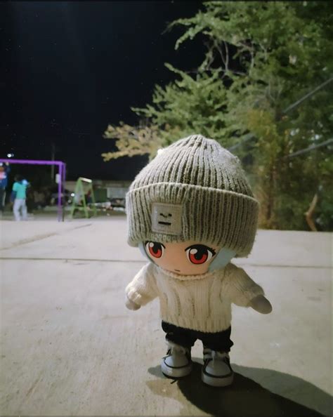 A Small Doll Wearing A Knitted Hat And Sweater Standing In Front Of A